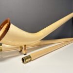 Alphorn mit hochwertigen Holzmundstücken auf weißem Tisch, ideal für NATURINSTRUMENTE Heimatklang, zeigt Handwerkskunst.