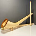 Hochwertiges Alphorn mit edlem Holzmundstück, präsentiert vor schlichter grauer Wand. Ideal für authentischen Heimatklang.