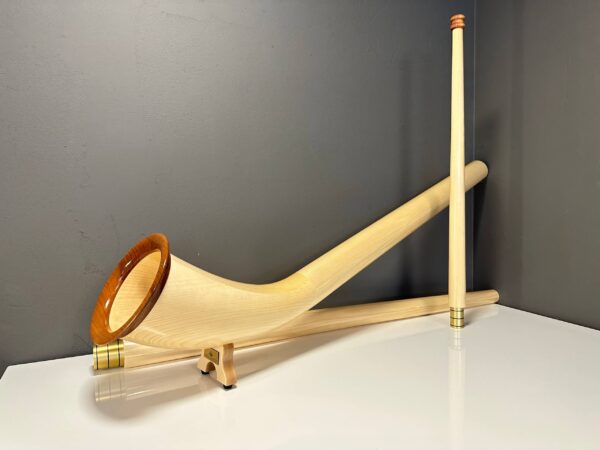 Hochwertiges Alphorn mit edlem Holzmundstück, präsentiert vor schlichter grauer Wand. Ideal für authentischen Heimatklang.