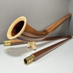 Alphorn aus edlem Holz mit präzise gearbeiteten Mundstücken, präsentiert auf weißer Oberfläche in modernem Raum.