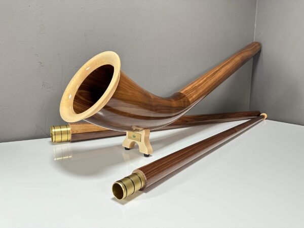 Alphorn aus edlem Holz mit präzise gearbeiteten Mundstücken, präsentiert auf weißer Oberfläche in modernem Raum.