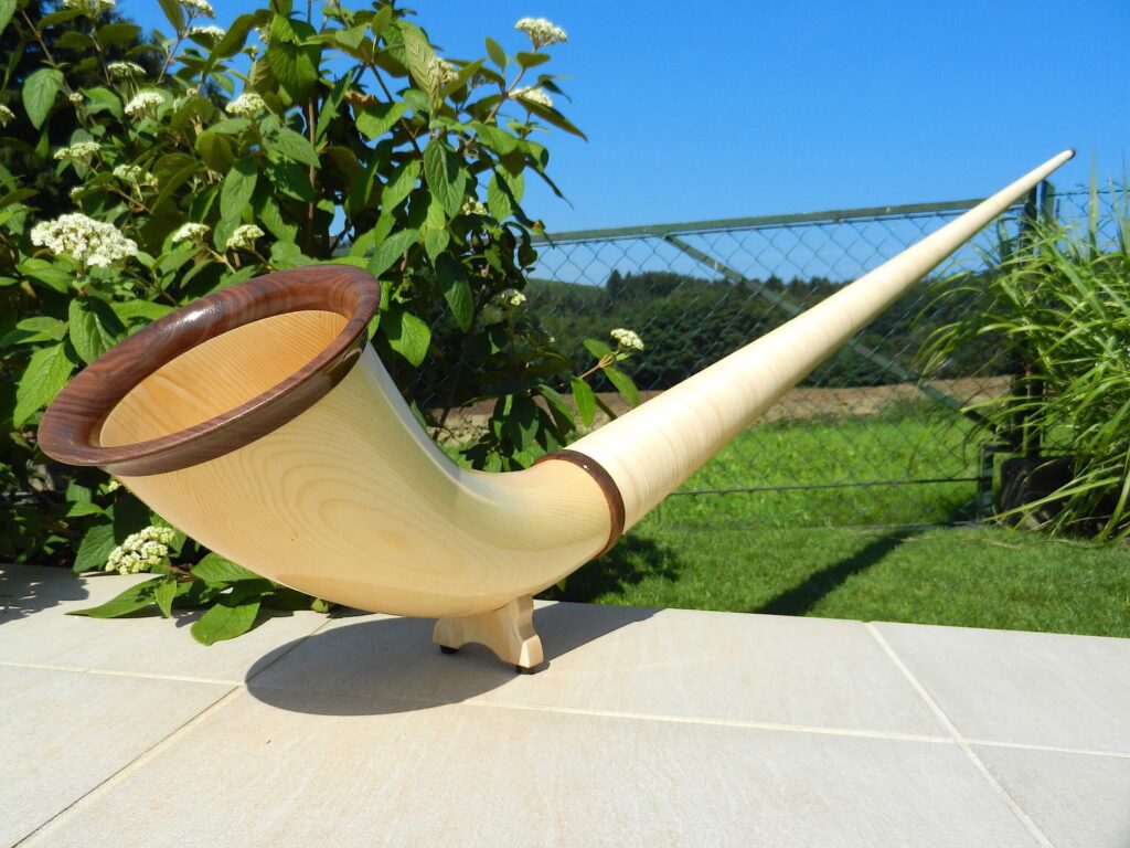 Elegant wooden alphorn with detailed mouthpiece, presented in a sunny garden, ideal for NATURINSTRUMENTE Heimatklang.