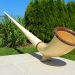 Elegantes Alpenhorn aus Holz auf einer Terrasse, umgeben von grüner Natur, ideales Instrument für den Heimatklang.