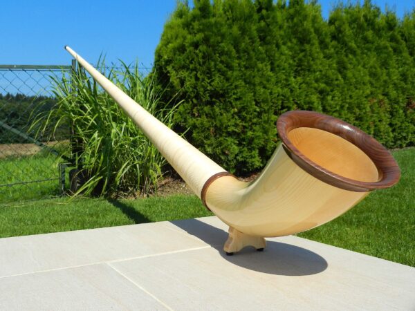 Elegantes Alpenhorn aus Holz auf einer Terrasse, umgeben von grüner Natur, ideales Instrument für den Heimatklang.