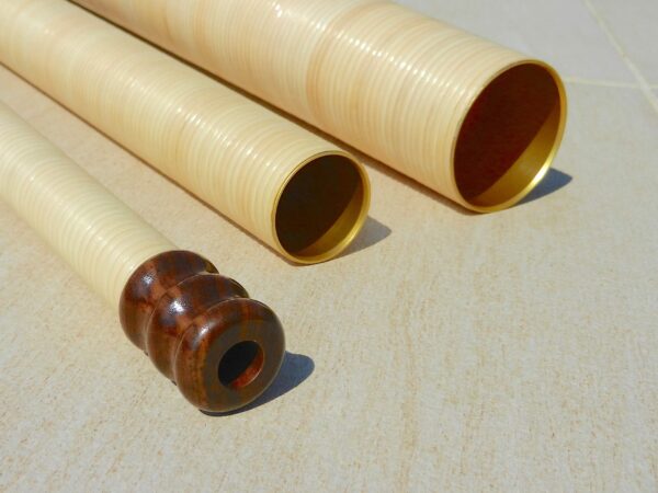 Hochwertige Alphorn-Rohre und Holzmundstück auf Steinboden, präsentiert von NATURINSTRUMENTE Heimatklang.