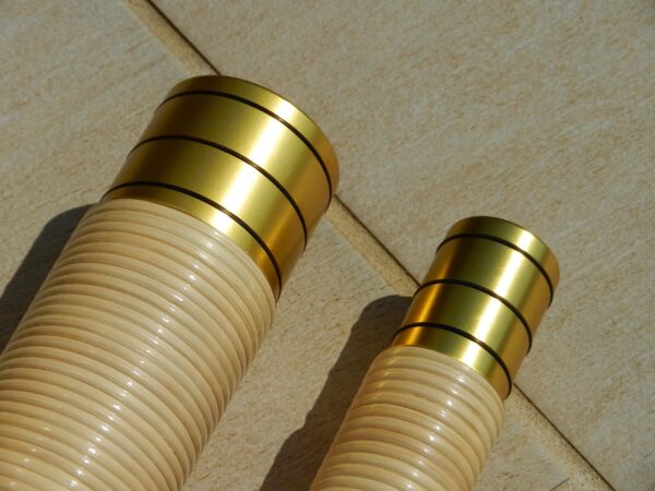 Zwei hochwertige Holzmundstücke für Alphörner, verziert mit goldenen Ringen, liegen auf einer Holzoberfläche.