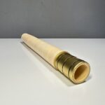 Handgefertigtes Alpenhorn-Mundstück aus Holz mit goldenen Details auf einem weißen Tisch, präsentiert von NATURINSTRUMENTE Heimatklang.