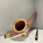 Hochwertiges Alpenhorn aus Holz, präsentiert mit handgefertigten Mundstücken auf einem Studiohintergrund für NATURINSTRUMENTE Heimatklang.