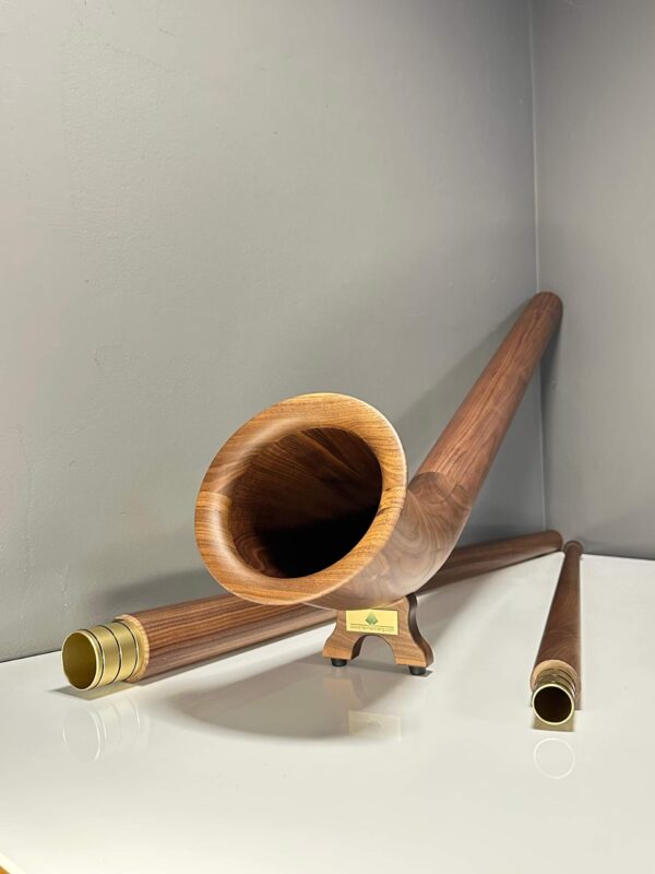 Hochwertiges Alpenhorn aus Holz, präsentiert mit handgefertigten Mundstücken auf einem Studiohintergrund für NATURINSTRUMENTE Heimatklang.