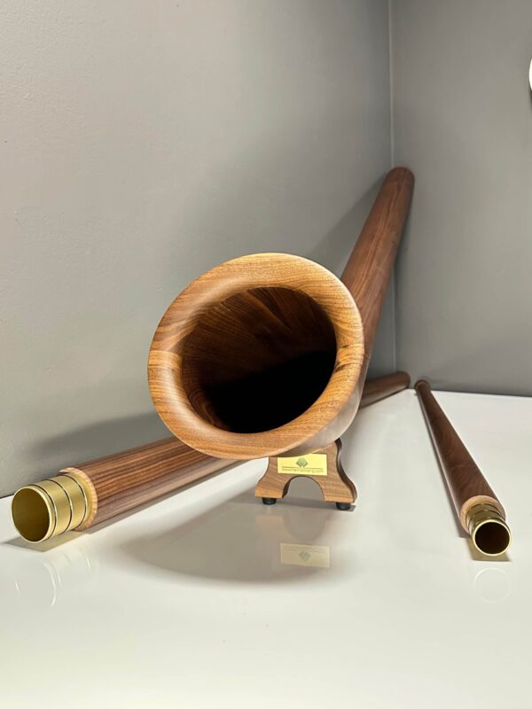 Alpenhorn auf Holzständer mit goldfarbenen Mundstücken, präsentiert auf glänzendem Tisch vor grauem Hintergrund.