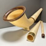 Alphorn mit Holzmundstück und Zubehör auf weißem Tisch vor grauer Wand.