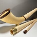 Hochwertiges Alphorn aus hellem Holz mit Zubehör, darunter abnehmbares Mundstück, präsentiert auf einem Tisch.