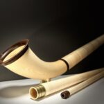 Alphorn mit stilvollem Holzmundstück präsentiert sich auf heller Oberfläche vor dunkelgrauem Hintergrund.