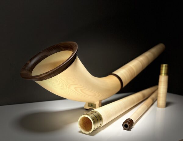 Alphorn aus hellem Holz mit Mundstück und Zubehör auf weißem Untergrund, gefertigt für Heimatklang Naturinstrumente.