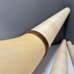 Detailaufnahme hochwertiger Alphörner aus Holz mit dunklem Mundstück, präsentiert vor grauem Hintergrund.