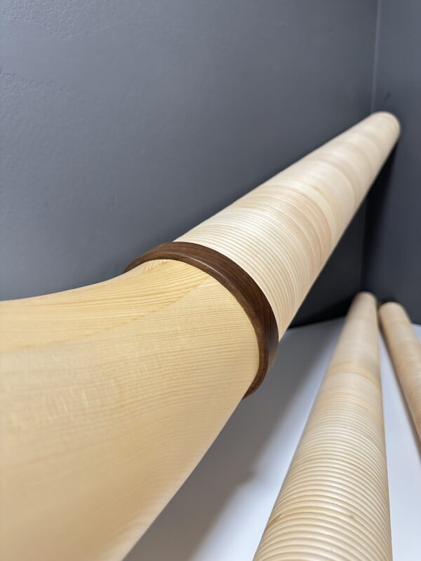 Detailaufnahme hochwertiger Alphörner aus Holz mit dunklem Mundstück, präsentiert vor grauem Hintergrund.