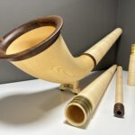 Handgefertigtes Alphorn mit Holzmundstück und weiteren Zubehörteilen, präsentiert auf weißer Fläche vor grauem Hintergrund.