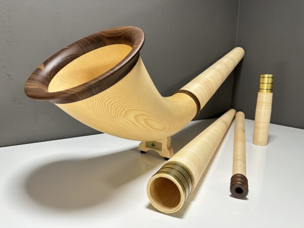 Handgefertigtes Alphorn mit Holzmundstück und weiteren Zubehörteilen, präsentiert auf weißer Fläche vor grauem Hintergrund.