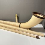 Alphorn mit Holzmundstücken auf weißem Tisch, ideal für Alpklänge und als hochwertiges Alphorn Zubehör.