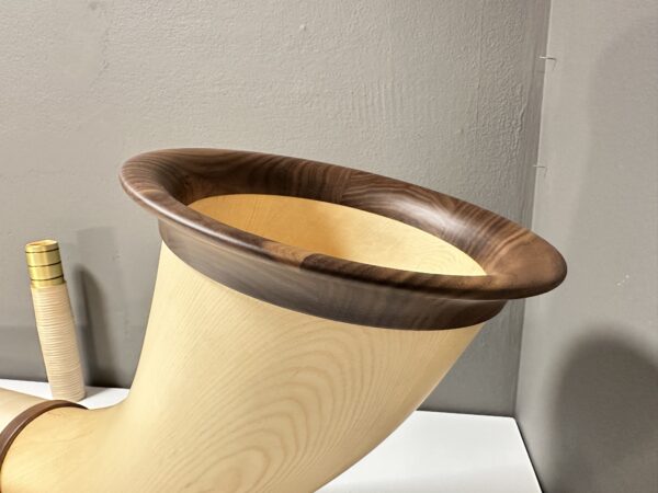 Alphorn aus hochwertigem Holz mit elegantem Mundstück, präsentiert vor neutraler Wand.