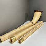 Alphorn aus hellem Holz mit hochwertigem Mundstück und Zubehör auf weißem Tisch.