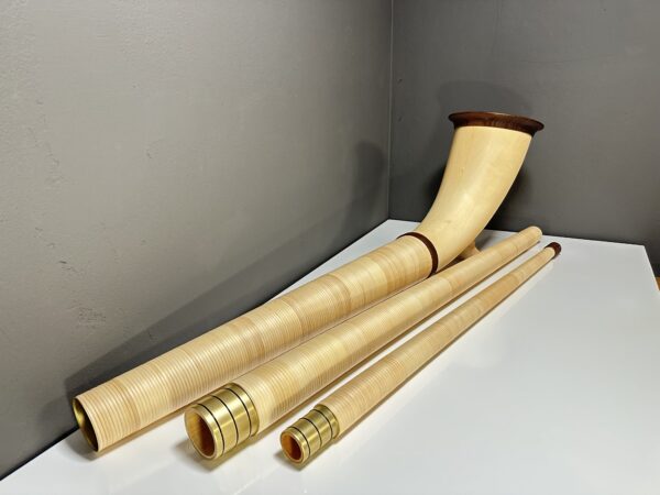 Alphorn aus hellem Holz mit hochwertigem Mundstück und Zubehör auf weißem Tisch.